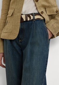 Denim jeans i mørkeblå med en avslappet passform, parret med en beige herringbone blazeren og et flerfarget mønstret belte.