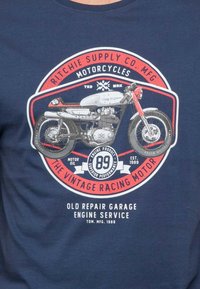 T-shirt bleu marine avec un graphisme de moto vintage en gris et rouge, comprenant des éléments textuels détaillés, un design de badge circulaire et une esthétique rétro.