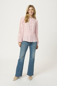 Blouse rose clair avec boutons sur le devant et manches ballon, ornée de motifs floraux brodés ; accompagnée d'un jean bleu évasé et de talons beiges.