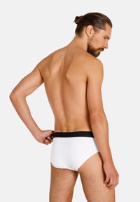 Weiße Herrenunterhosen mit einem schwarzen elastischen Bund, glattem Stoff und einem minimalistischen Design. Von hinten gezeigt, um Passform und Form hervorzuheben.