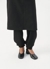 Pantofi negri cu toc, cu un model texturat de crocodil, asortați cu pantaloni negri largi cu tivuri răsucite și un articol vestimentar negru cu croială dreaptă deasupra.