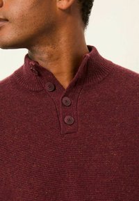 Burgunderfarbener Strickpullover mit geripptem Kragen, Knopfleiste mit drei Knöpfen, strukturiertem Stoff und dezenten Farbakzenten.