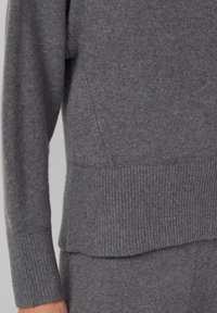 Pull gris en maille avec poignets et ourlet côtelés, présentant une texture douce et une coupe décontractée, avec des coutures détaillées sur les côtés.