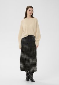 Pull en tricot beige à manches longues associé à une jupe midi noire à pois. La tenue présente une texture lisse et une coupe décontractée.