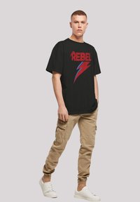 Black t-shirt with bold red "REBEL" text and blue lightning bolt design. Paired with beige cargo pants and white sneakers.