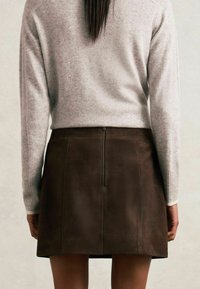 Barna velúr szoknya sima felülettel és hátsó cipzárral. Egy világosszürke pulóverrel párosítva, amely laza szabású és bordázott mandzsettákkal rendelkezik.