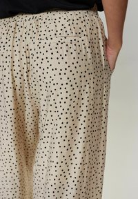 Beige palazzobroek met een zwart stippenpatroon, een elastische tailleband en zijzakken. De textuur lijkt glad en lichtgewicht.