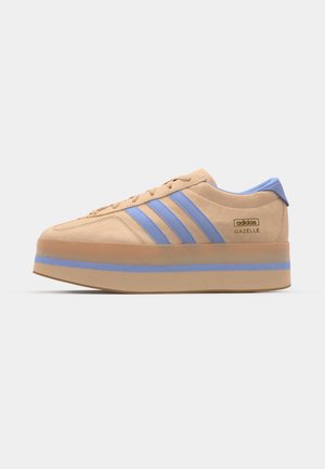 Sneaker beige in suede con strisce azzurro, suola piatta e dettagli blu sul tallone. Presenta una chiusura con lacci e un logo laterale.