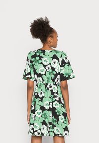 Vestido floral em preto com grandes flores verdes e brancas. Mangas curtas, cintura franzida, tecido macio e um corte relaxado.