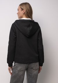 Czarna bluza z kapturem o miękkiej teksturze, z delikatnym błyszczącym detalem na plecach. W zestawie z szarymi dżinsami.