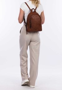 Brązowy skórzany plecak o zaokrąglonym kształcie, z regulowanymi paskami i górnym uchwytem. Posiada zasuwaną kieszeń z boku oraz teksturowane wykończenie.