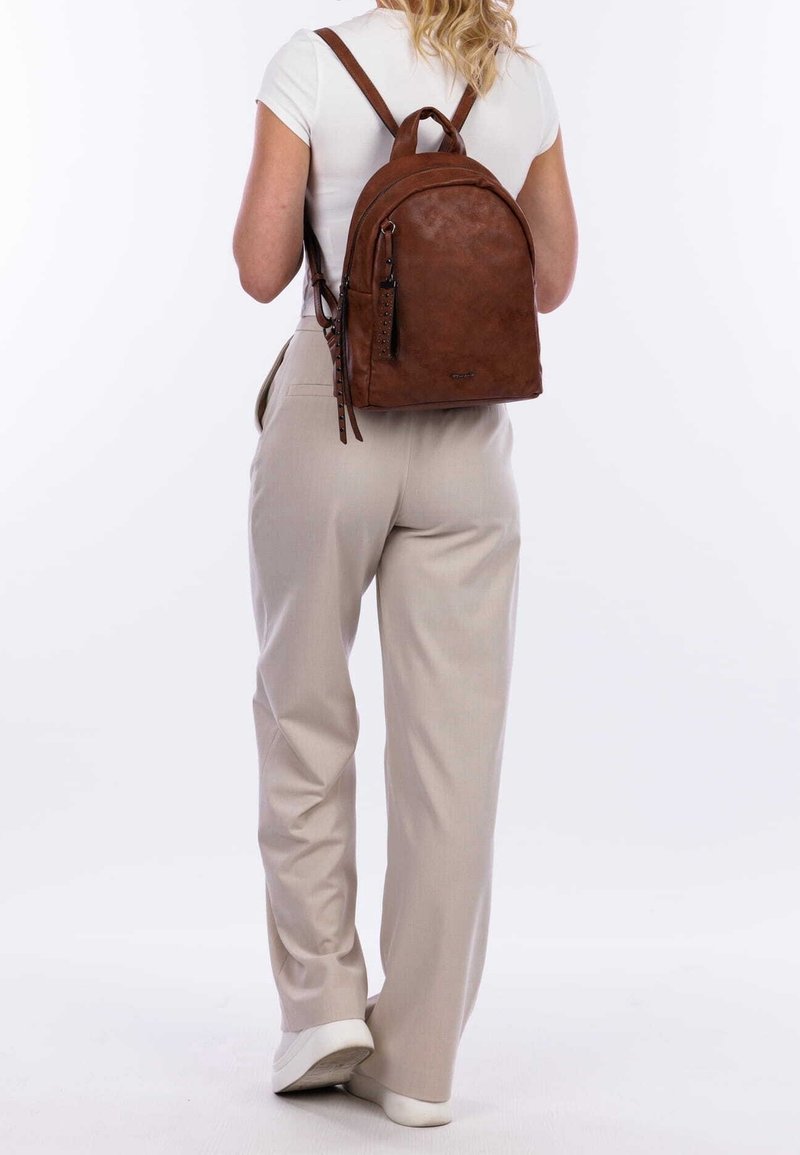 Brązowy skórzany plecak o zaokrąglonym kształcie, z regulowanymi paskami i górnym uchwytem. Posiada zasuwaną kieszeń z boku oraz teksturowane wykończenie.