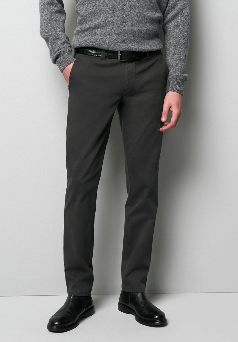 Dark gray chinos made of fabric with a smooth texture, featuring a slim fit, side pockets, and a belt with a shiny buckle. Black ankle boots.