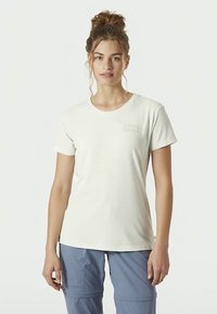 Světlé šedé tričko s krátkým rukávem, kulatým výstřihem a decentním logem na hrudi. Měkká látka a volný střih, spojené s modrými kalhotami.