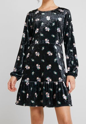 Robe en velours noir avec de longues manches bouffantes, imprimé floral en rose et vert, ourlet à volants, encolure ronde. Texture douce et coupe décontractée.