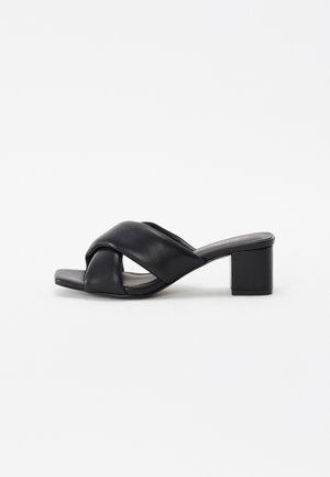 Sort læder mule sandal med åben tå, brede krydsede remme og en blokhæl i mellemhøjde på hvid baggrund.
