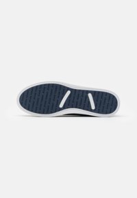 La suola nera delle sneakers presenta una gomma blu testurizzata con un motivo di testo "TOMMY JEANS", bordi bianchi e due ritagli circolari per la flessibilità.