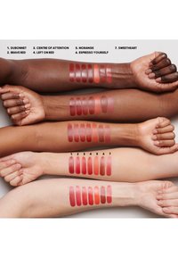 Swatches of seven lip colors displayed on three arms of varying skin tones. Colors range from deep red to soft pink, with glossy and matte finishes.
