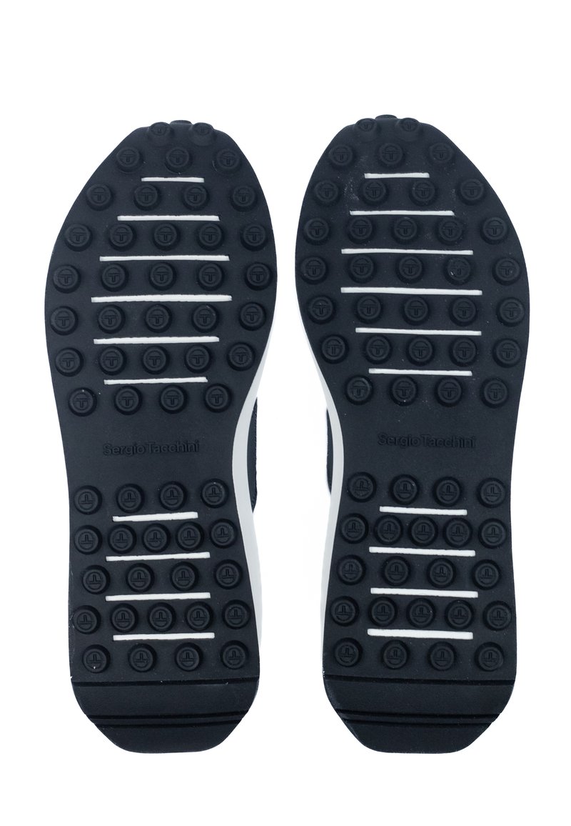 Suela de zapato de goma negra con acentos blancos, con múltiples puntos de tracción circulares y ranuras horizontales para mayor agarre y durabilidad.