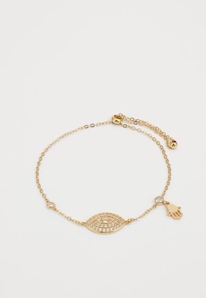 Zlatna narukvica s članom u obliku oka koji ima prozirne rhinestones, malim okruglim akcentom i detaljem u obliku ruke.