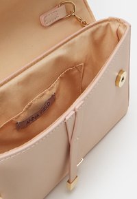 Sac à main synthétique rose avec ferrures dorées, intérieur en satin, et une étiquette portant la mention "ANNA FIELD." Comprend une poche intérieure et une fermeture à pression.