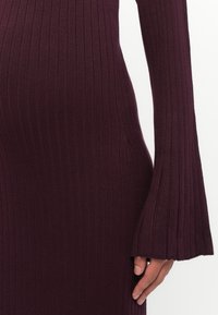 Abito midi a costine in magenta profondo, con maniche lunghe e polsini a campana. Il materiale ha una consistenza morbida e una silhouette aderente.