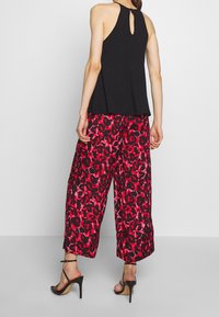 Schwarzes ärmelloses Top mit einem Schlüssellochdetail im Rücken, kombiniert mit weit geschnittenen Hosen, die ein rot-schwarzes Tiermuster aufweisen.