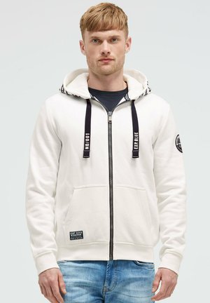 White zip-up hoodie with a drawstring hood, front pockets, and a fabric label. Features a smooth texture and contrasting dark zipper.
