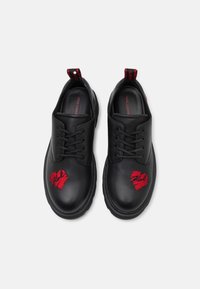 Chaussures à lacets en cuir noir avec des motifs de cœurs brodés en rouge sur chaque bout, semelles texturées noires et languettes de tirage contrastantes rouges.