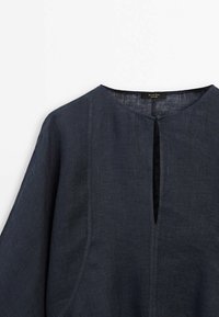 Top in lino blu scuro con scollatura rotonda, fessura frontale e maniche larghe. Presenta una texture sottile ed elementi di design minimalisti.