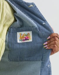Giacca di jeans a strisce blu e bianche, con un'etichetta multicolore vivace in una tasca a toppa. L'interno è in un tessuto beige uniforme.