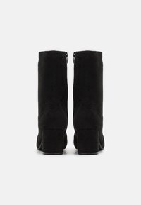 Bottines en suède noir avec un talon épais, présentant une texture lisse et une fermeture éclair à l'arrière pour un enfilage facile.