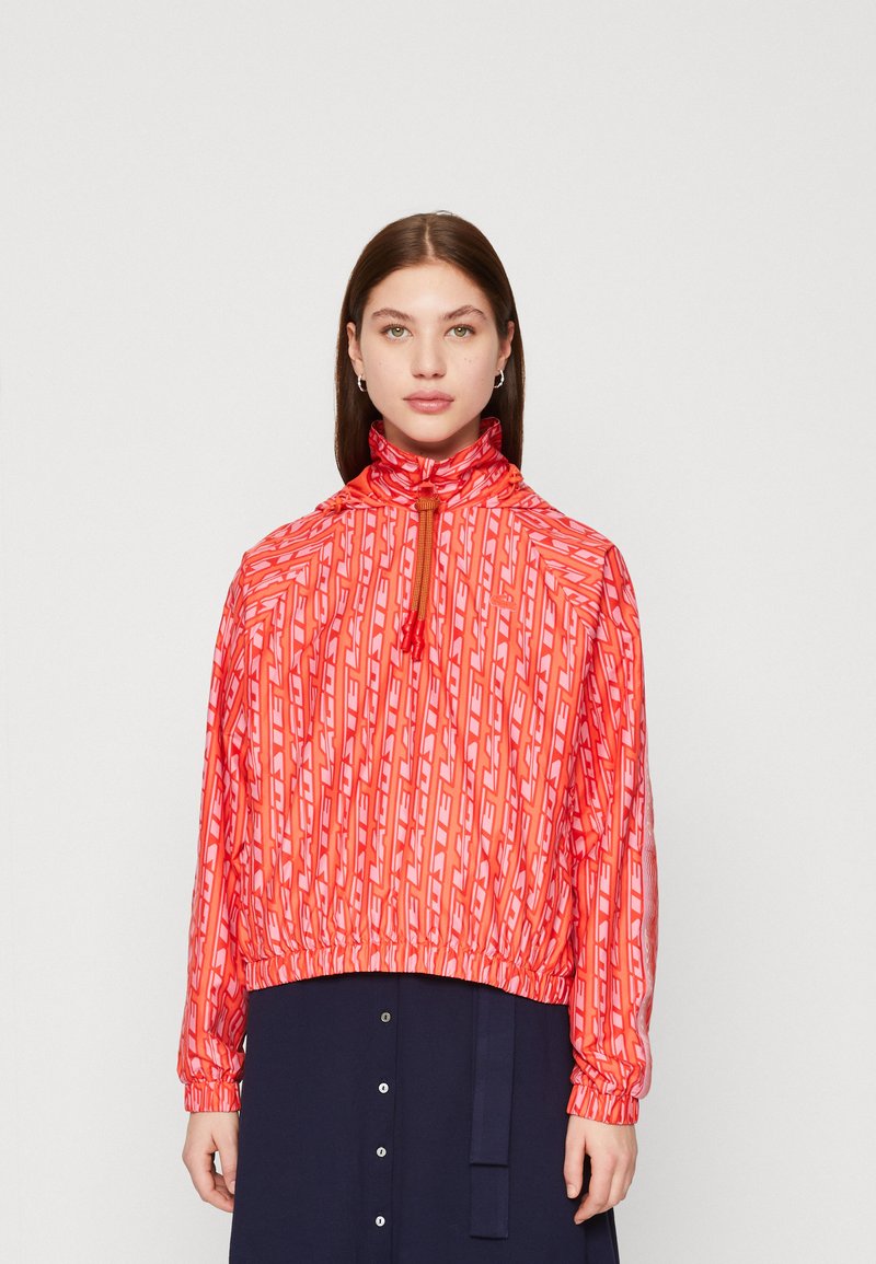 Giacca rossa con motivo a stampa e colletto alto, orlo e polsini elasticizzati. Presenta una mezza zip e design geometrico in tonalità di rosa e bianco.