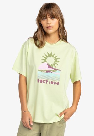 Svetlozelené tričko z bavlny s grafickým potlačou so slnkom, horami a nápisom "ROXY 1989" v purpurovej a ružovej farbe. Voľný strih.