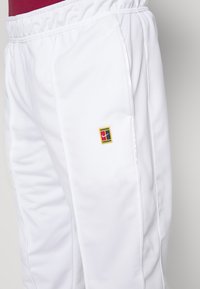 Witte sportbroek met een elastische tailleband, voorzien van een klein multicolor logo op de dij en een gladde textuur.