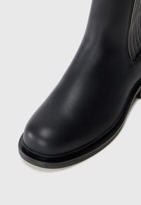 Black leather ankle boot with a smooth finish, rounded toe, and subtle stitching detail along the side. Sturdy sole and minimal design.