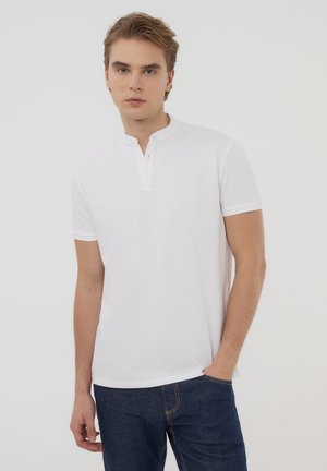 Polo bianco a maniche corte con colletto rialzato e due bottoni. Tessuto di cotone liscio, abbinato a jeans in denim blu scuro.