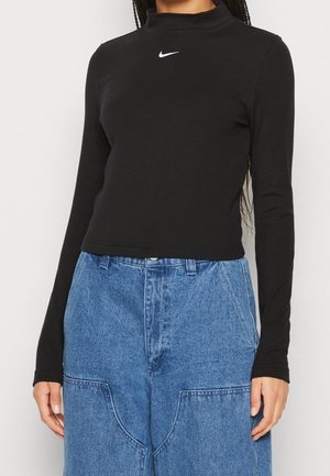 Maglietta nera a maniche lunghe con collo alto in un tessuto a costine, con il logo Nike bianco sul petto, abbinata a pantaloni in denim azzurro chiaro a gamba larga.