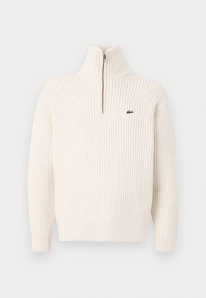 Crème-kleurige textuur gebreide trui met een kwart ritssluiting en een klein groen geborduurd krokodillenlogo op de borst.