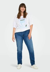 Balta trumpa rankovėmis marškinėliai su pasteliniu kavinių grafikų piešiniu ir mėlynomis džinsinėmis kelnėmis. Modelis, dėvintis baltas sportines batus, stovi prieš paprastą foną.