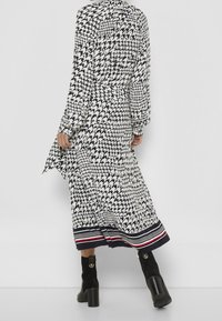 Långärmad klänning i svart och vitt hounds-tooth-mönster, med en utsvängd nederkan och marinblå randiga detaljer i botten. Tillsammans med svarta ankelboots.