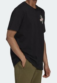 Černé bavlněné tričko s kulatým výstřihem, krátkými rukávy a grafickým potiskem na přední straně se vzorovaným designem v bílých a růžových tónech.