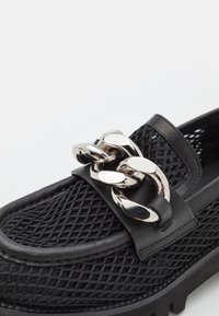 Mocassin en mesh noir avec détail chaîne argentée épaisse sur le dessus et bordure en cuir noir.