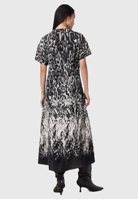 Vestido maxi en blanco y negro con estampado animal, mangas cortas y detalle de abertura en la espalda. Textura suave, silueta fluida.