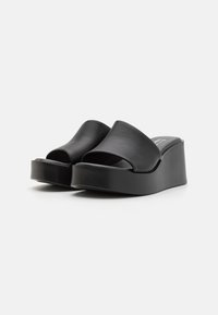 Sandales à plateforme noires en cuir lisse, avec un design à bout ouvert et une semelle épaisse en wedge pour plus de hauteur.