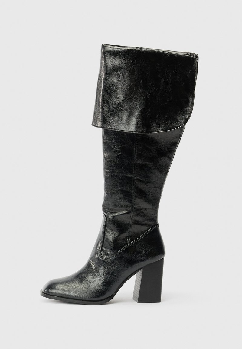 Bota de couro preta até ao meio da panturrilha com o topo dobrado e salto bloco, apresentada de lado sobre um fundo branco liso.