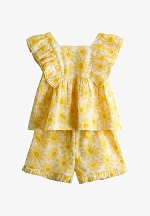 Sárga virágmintás ujjatlan felső fodros vállrésszel és hozzá illő fodros rövidnadrág gyerekeknek, fehér háttéren.