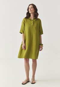 Rochie din in verde lime, cu mâneci scurte, placket cu nasturi, croială lejeră și tiv până la genunchi. Purttă cu sandale bej și brățări.