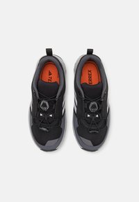 Black athletic shoes with a mesh upper, gray accents, and orange insoles. Features a lace-lock system and a padded collar.