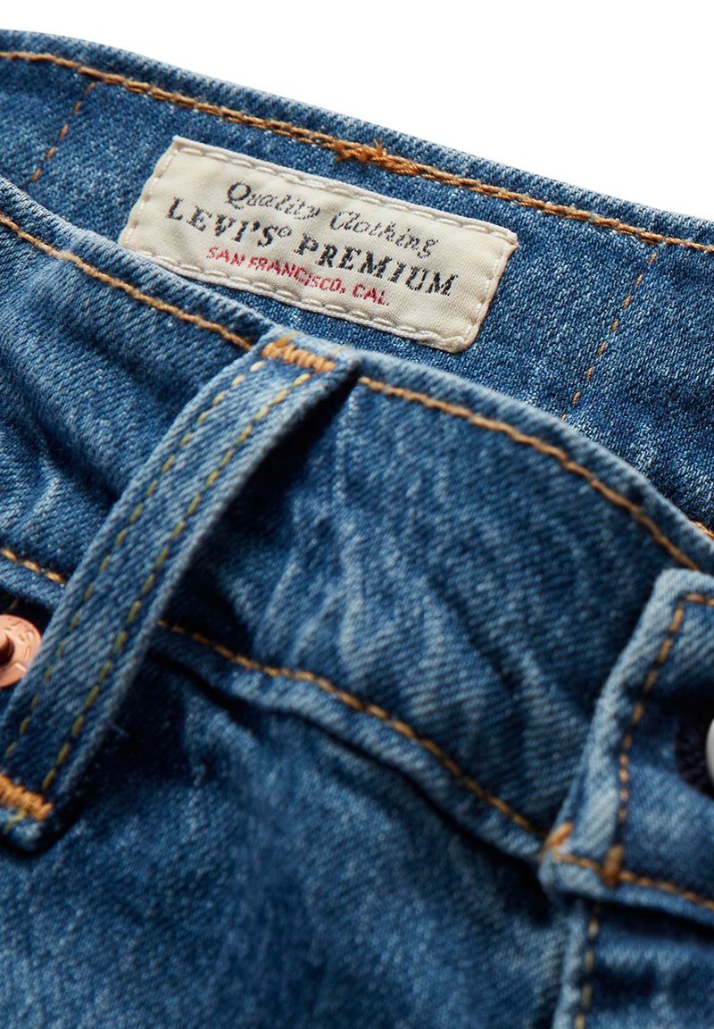 Jean en denim avec une finition bleu foncé, dotés de coutures orange contrastantes et d'une étiquette en cuir portant l'inscription "Levi's Premium" au niveau de la taille.